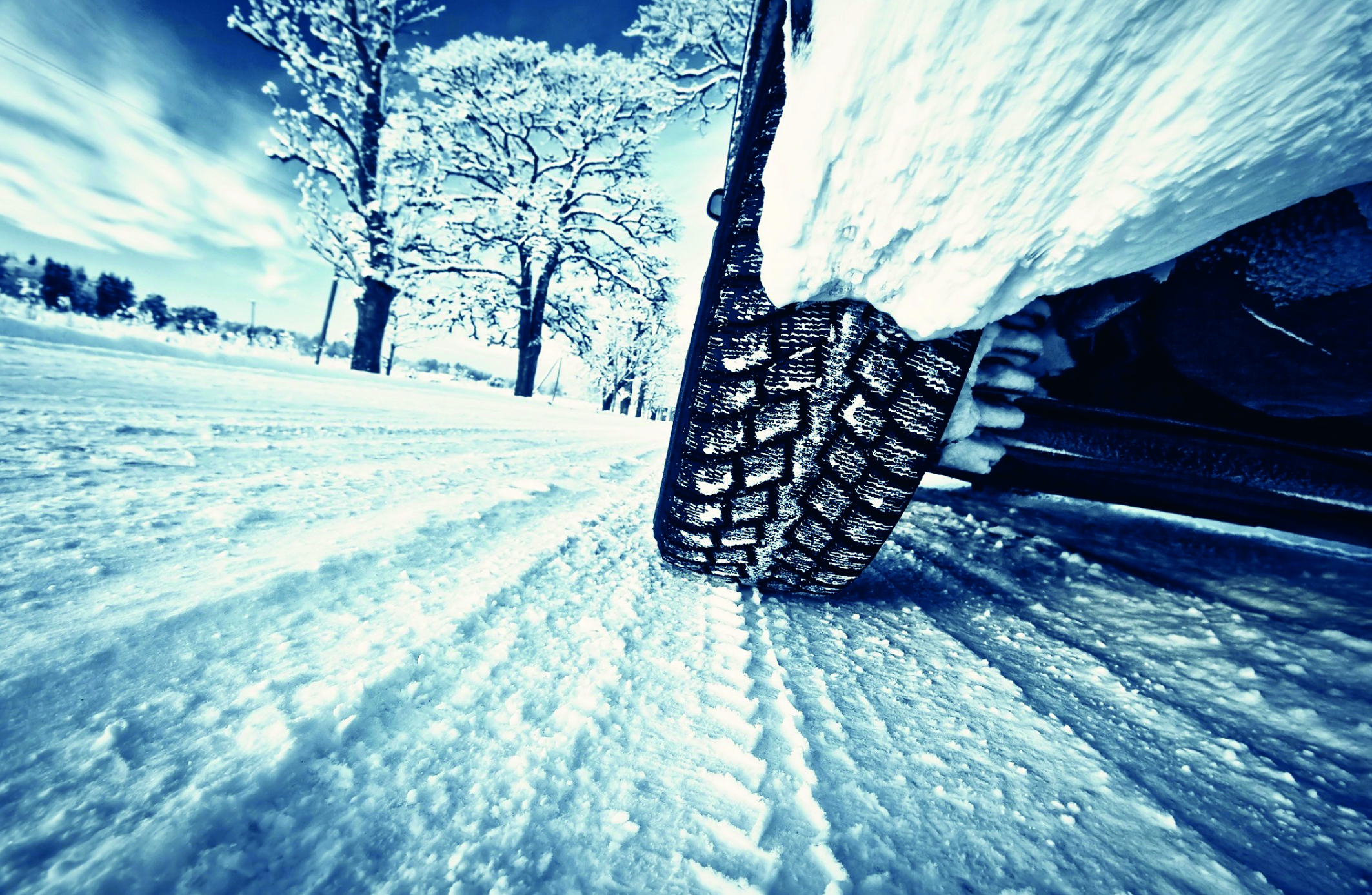 Nahaufnahme eines Mietwagen mit Winterreifen auf schneebedeckter Fahrbahn (Winterreisen).