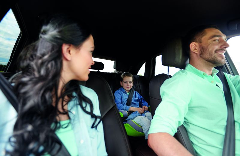 Eine Familie fährt gemeinsam im Auto. Die Frau schaut zurück auf die Rückbank zu einem kleinen Jungen (Fahrzeug prüfen)