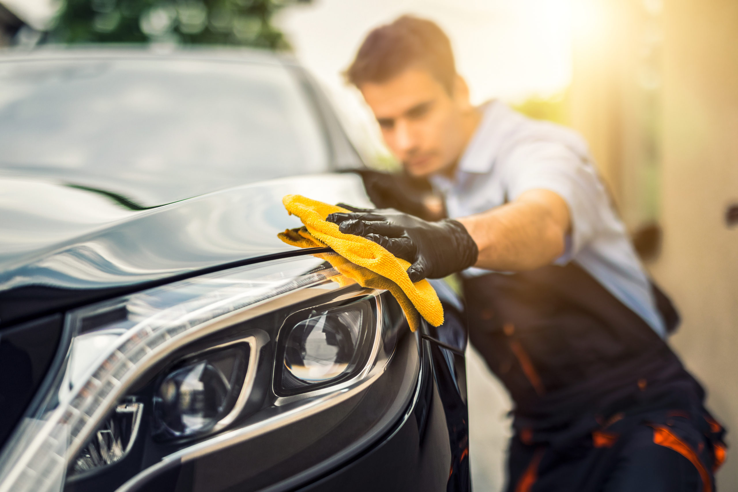 Regelmäßige Autopflege: ein Mann poliert sein Auto mit einem gelbem Tuch.