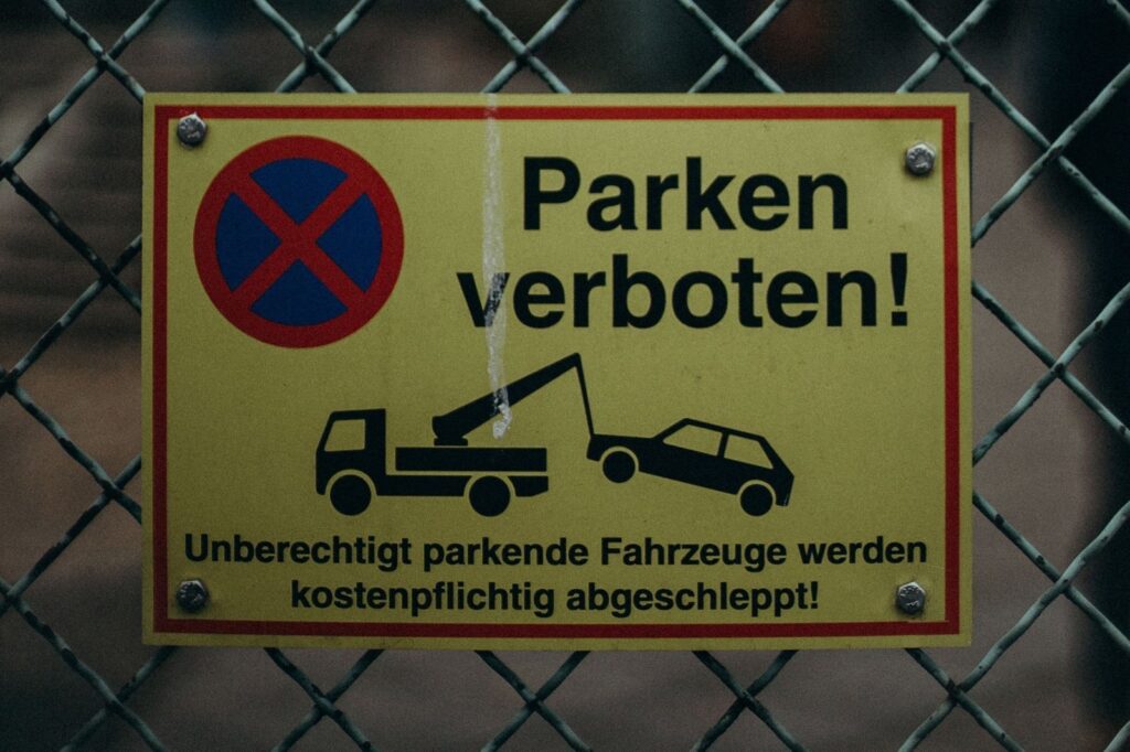 Gelbes Schild am Zaun: Parken verboten, unberechtigt parkende Fahrzeuge werden kostenpflichtig abgeschleppt