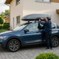 Dachbox montieren: ein modernes Auto mit geschlossener Dachbox auf dem Grundträger, eine Person prüft den Verschluss